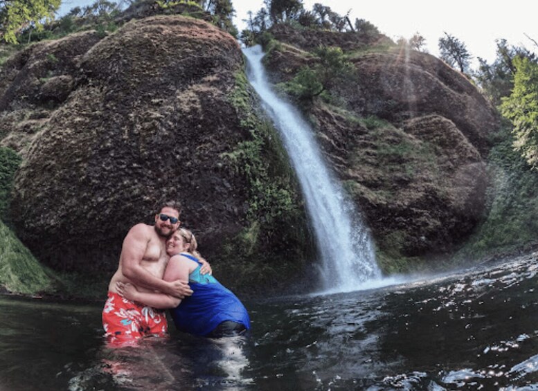 A couple embracing by a waterfall with a large rock formation in the background. 2