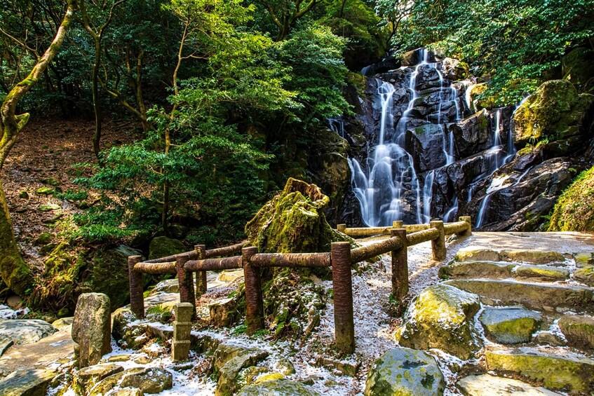 A waterfall cascading over rocks, surrounded by lush greenery and a wooden fence. 5