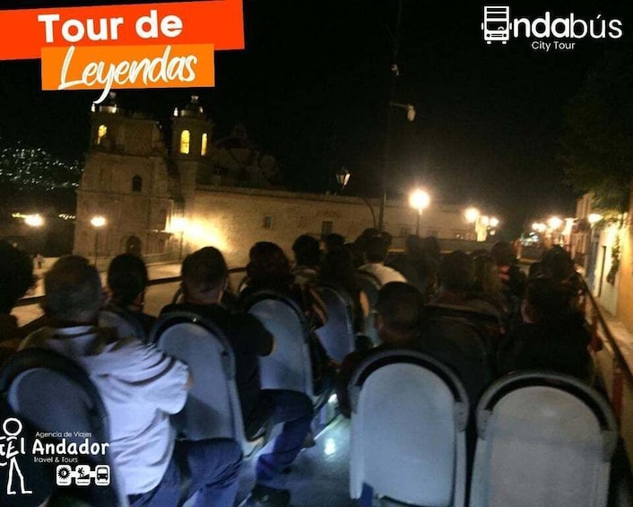 A group of people seated on chairs, facing a historic building with illuminated windows at night. 3