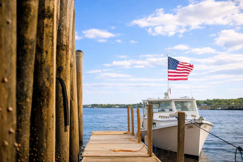 A wooden dock with a boat docked at the end, an American flag flying, and a clear blue sky. 3