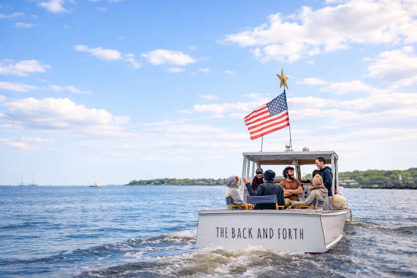A boat named 'The Back and Forth' with an American flag and a star on top, sailing on a body of water with a clear sky and distant land in the background. 2