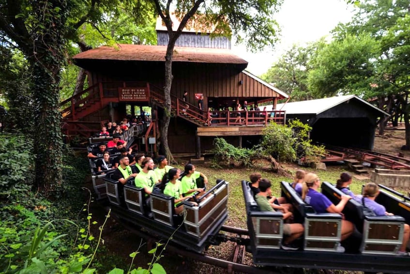 A group of people on a small train ride through a wooded area with a rustic building in the background. 3