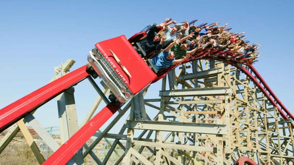 A wooden roller coaster with red cars in motion. 1