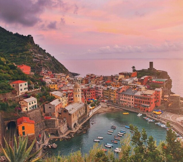 A coastal town with colorful buildings, a harbor with boats, and a hill with a fortification. 5