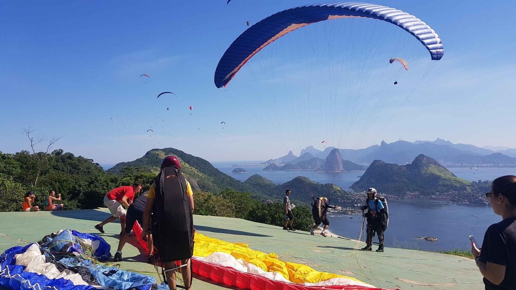 Un groupe de personnes se préparant à faire du parapente, avec une vue panoramique sur les montagnes et une ville en arrière-plan. 1