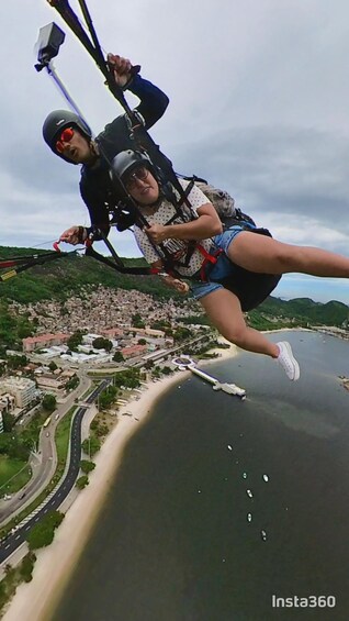 Une personne pratiquant le saut à l’élastique avec un parachute, surplombant un paysage urbain côtier avec une étendue d’eau et une route. 2
