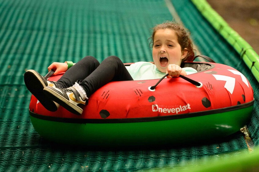 A child in a red and green inflatable tube, holding onto the handles, lying on a green mat. 5