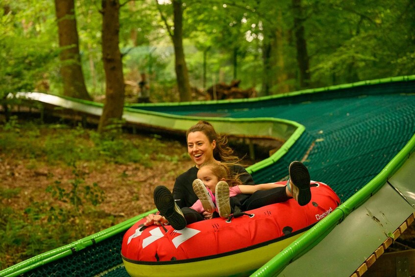 A person in a red inflatable tube sliding down a green slide in a forest. 4