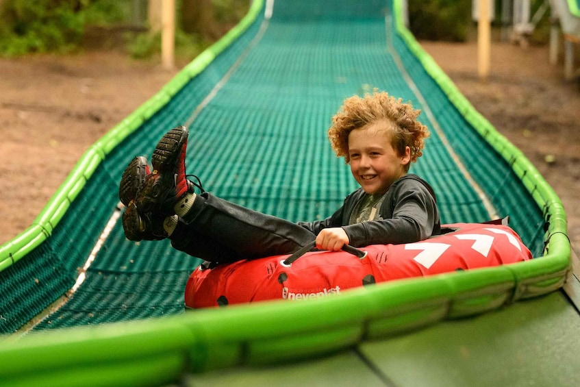 A child on a green slide with a red safety bag. 1