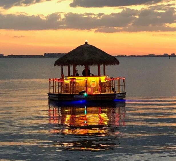 A boat with a thatched roof and illuminated interior, floating on calm water during sunset. 4