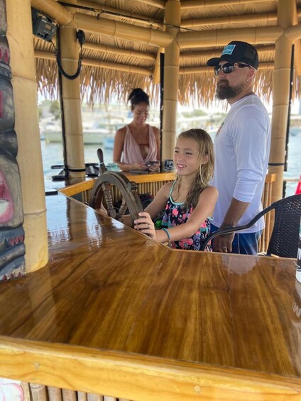 A wooden bar with a steering wheel, a person standing behind it, and a woman in the background. 1