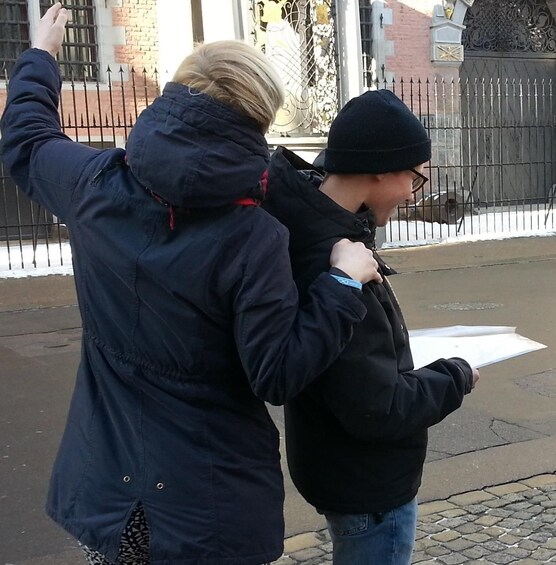 Two people standing on a street, one wearing a dark jacket and the other in a black coat. 4