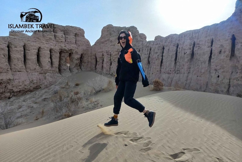 A person walking on a sandy terrain with rocky formations in the background. 5