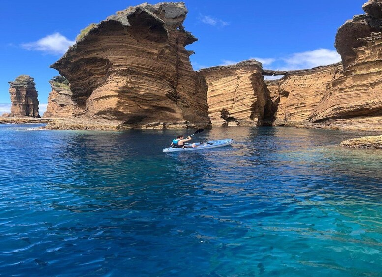 A kayaker on a clear blue sea with rock formations in the background. 5