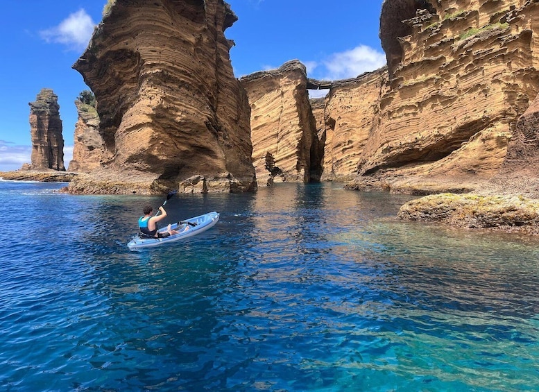 A kayaker in a clear blue sea with rocky cliffs in the background. 1