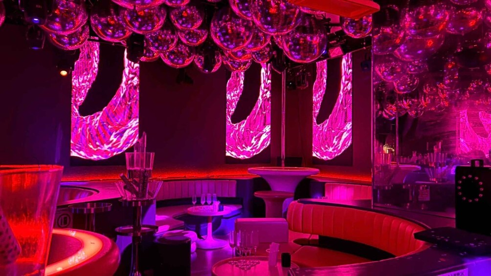A bar with purple lighting, round tables, and a red booth. 4