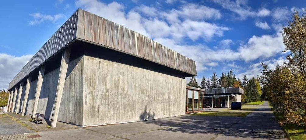 A modern building with a sloped roof and a concrete facade, set against a backdrop of trees and a clear sky. 3