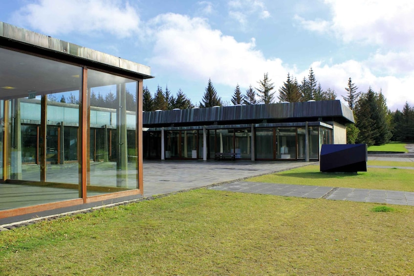 A modern building with large glass windows and a metal roof, surrounded by a grassy area and trees. 4