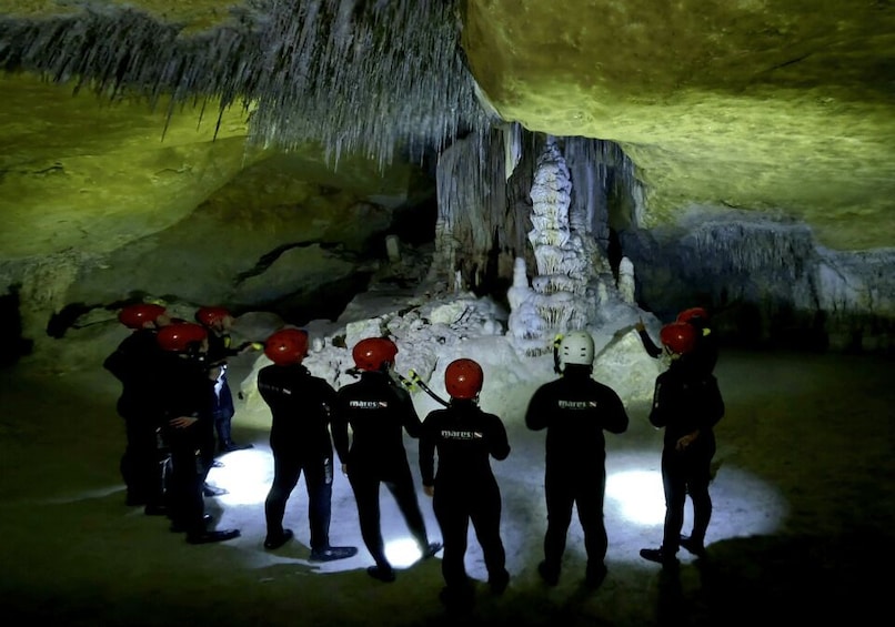 A group of people in helmets standing in a cave with stalactites. 4