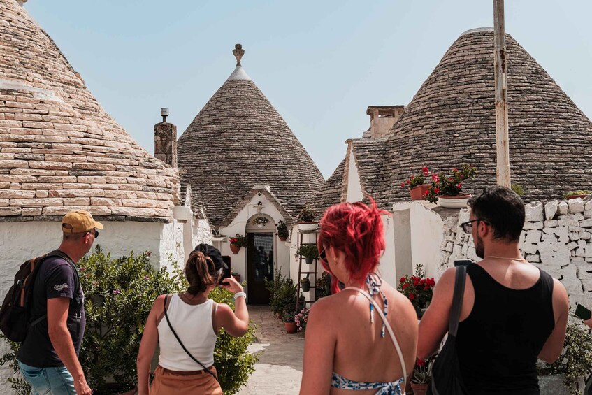 A group of people walking towards traditional stone houses with conical roofs. 3