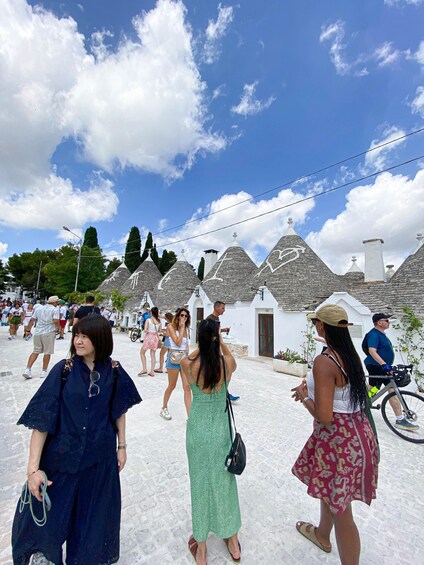 A group of people walking in a village with white buildings and stone roofs. 5