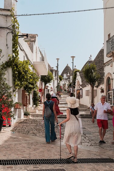 A cobblestone street in a historic town with white buildings, vines, and a clear sky. 1