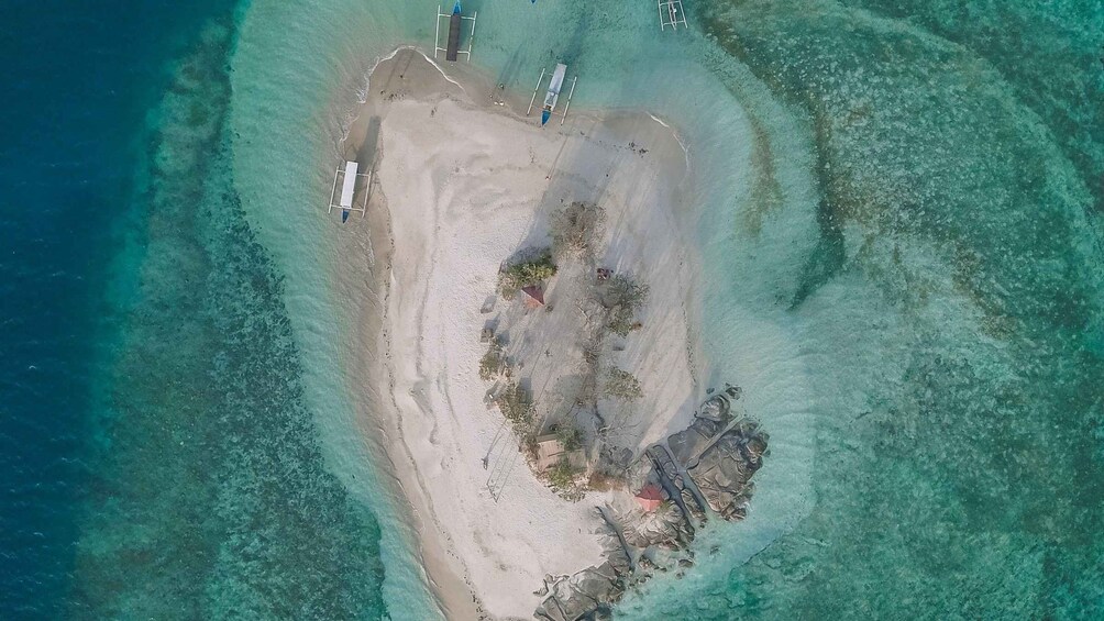 An aerial view of a beach with clear turquoise waters, a sandy shore, and some structures including a lifeguard tower and a small building. 2