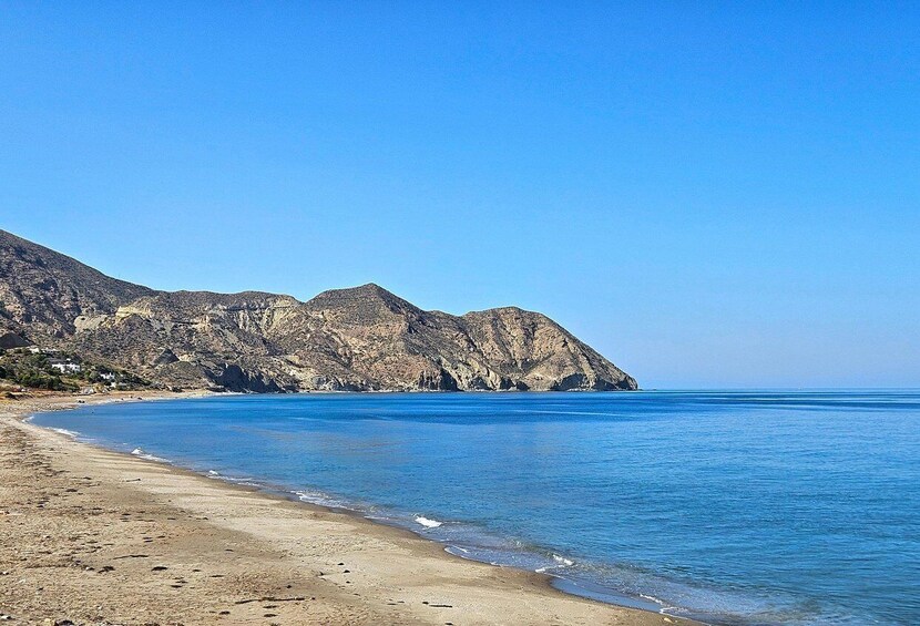 A beach with clear blue water, sandy shore, and rocky cliffs in the background. 4