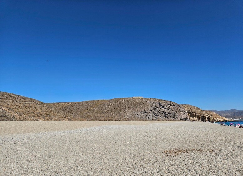 A desert landscape with a clear blue sky, rocky hills, and a gravelly foreground. 5