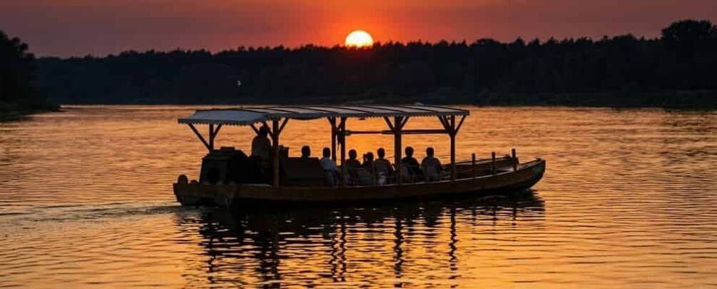 A boat with a covered deck on a calm body of water during sunset. 1