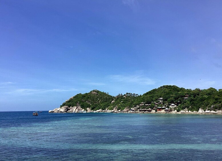 A coastal landscape with clear blue waters, a small boat, and a hill with buildings. 5