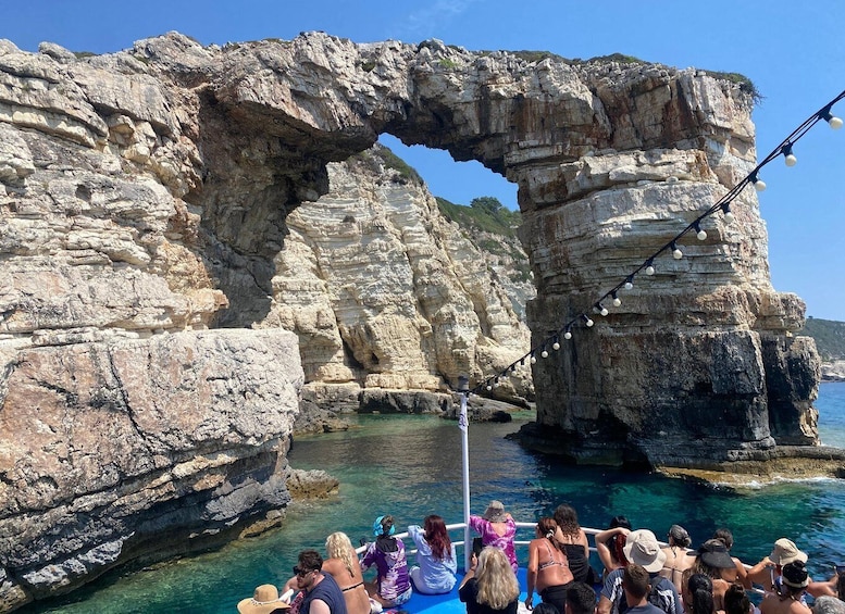 A group of people on a boat near a large rock formation with a natural arch. 5