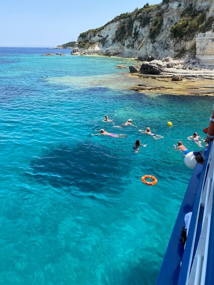 A group of people swimming in clear turquoise waters near a rocky coastline. 3