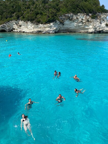 People swimming in a clear blue pool with a rocky coastline in the background. 2