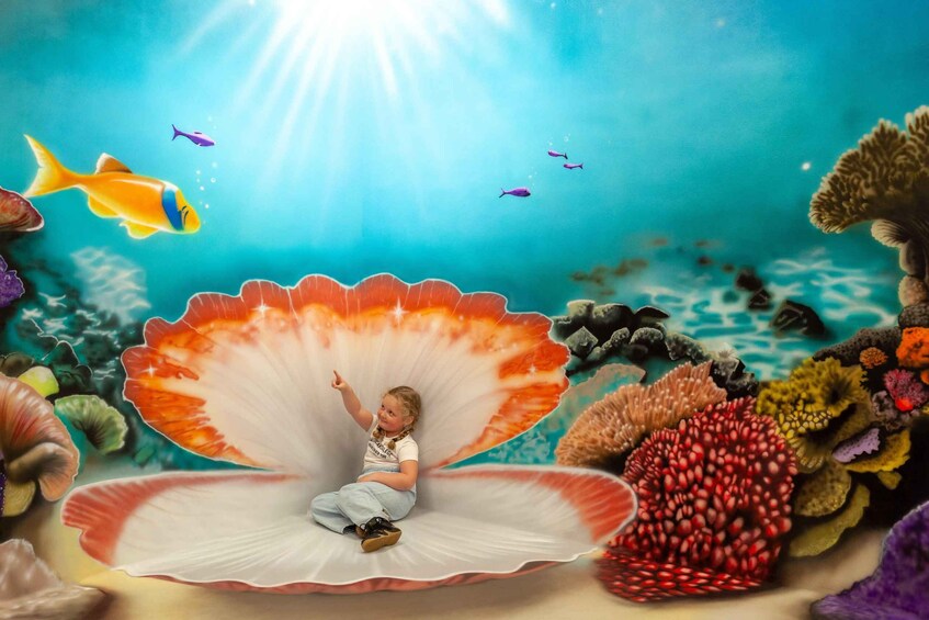 A child sitting on a seashell with fish and coral in the background. 5