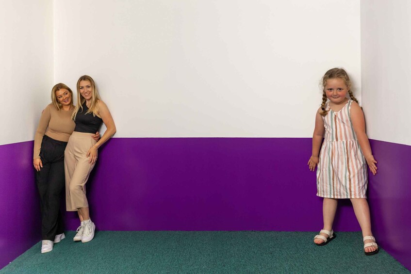 Three people standing against a purple wall with a green carpet. 3