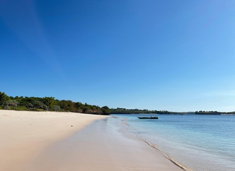 A beach with clear skies, calm waters, and a boat on the shore. 5