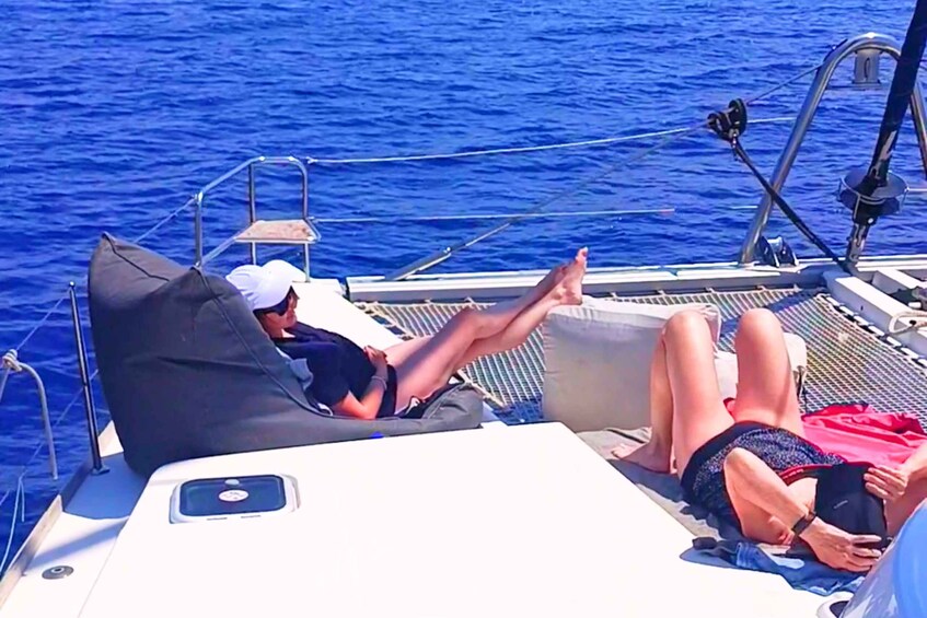 A boat with two people reclining on deck chairs, one wearing a white cap and the other in swimwear, with the ocean in the background. 5