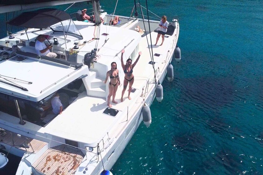 A sailboat with people on deck, a clear blue sea, and a person raising an arm. 4