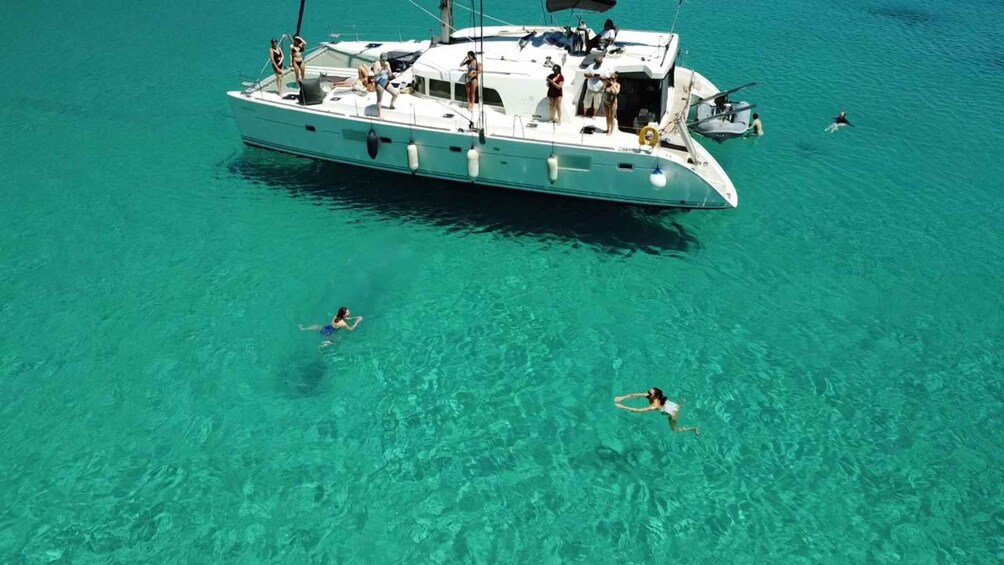 A white yacht with people on deck and two individuals swimming in clear turquoise water. 1