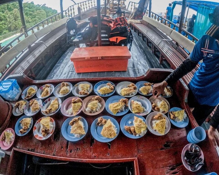 A boat deck with multiple plates of food, a red container, and a person serving food. 2