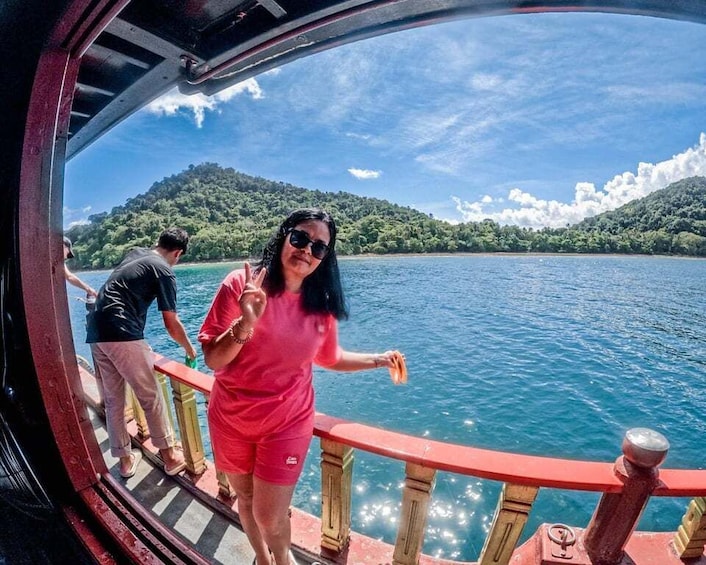 A person in a red shirt standing on a boat deck, looking out at a calm lake with a forested island in the distance. 5