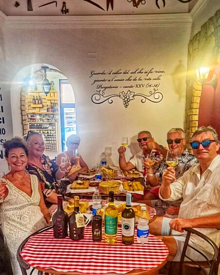 A group of people sitting around a table with wine bottles and glasses, in a restaurant with a decorative wall and a sign with a quote. 1