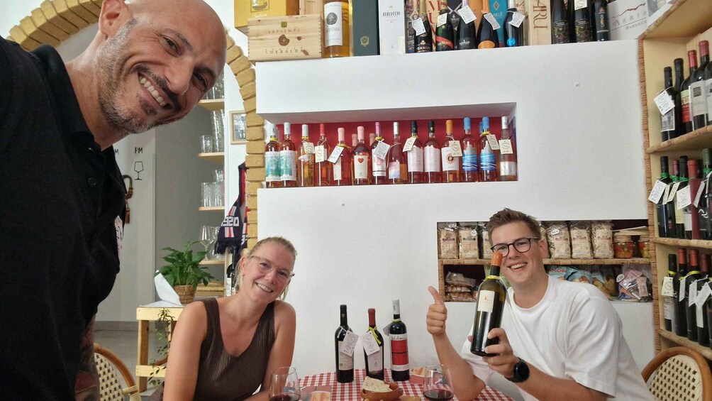 Three people seated at a table with wine bottles in a store. 3