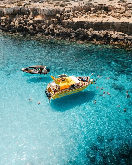 A clear blue sea with two boats, one yellow and one blue, and people swimming and sunbathing. 2