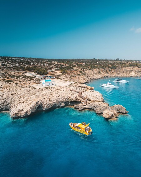 A coastal landscape with rocky terrain, a white building, and a yellow boat named 'Sirena One' on the water. 1