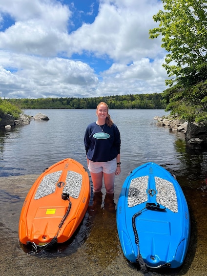 A person standing between two kayaks on a calm lake with a forested shoreline. 3