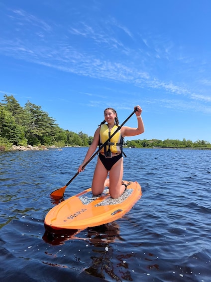 A person on a paddleboard in a body of water with trees and a clear sky in the background. 4