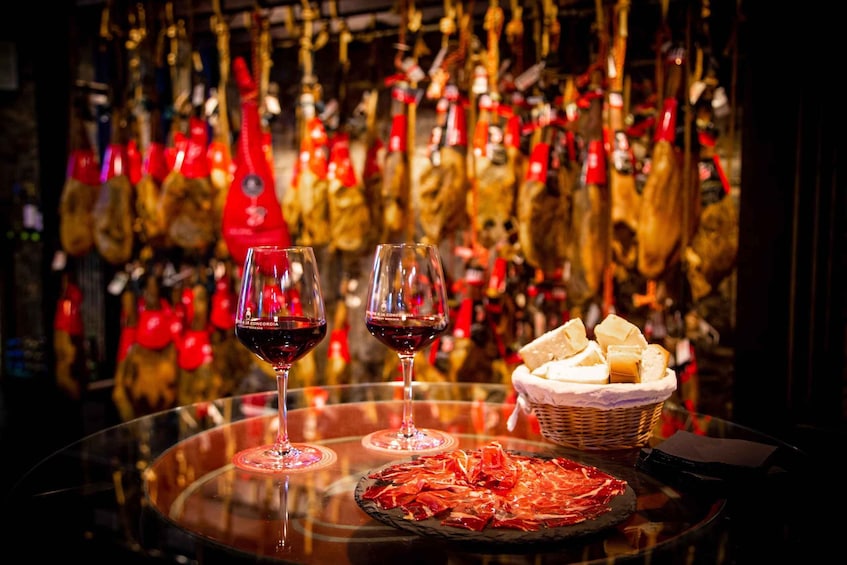 A glass table with two wine glasses, a plate of cured meat, and a basket of bread. 1