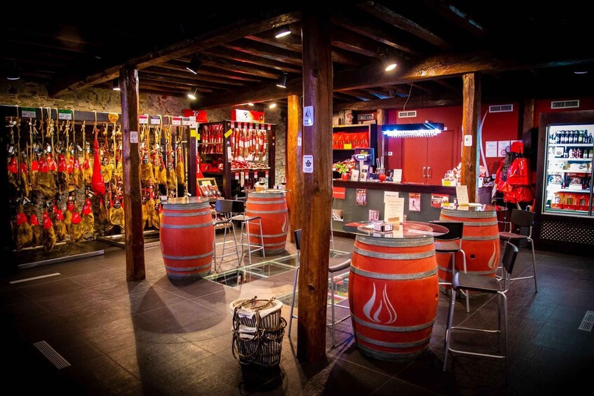 A rustic interior with wooden beams, red barrels, and a display of hanging sausages. 3